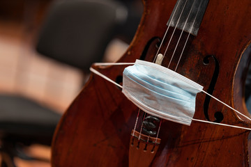 A face mask put over the bridge of a cello representing performance restrictions during a pandemic