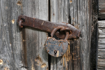 Close up view of the old rusty padlock on a aged gray wooden door