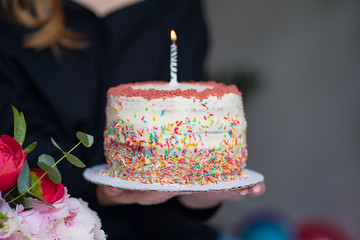 Close up of  woman holding a birthday cake with one candle and colourful sprinkles 