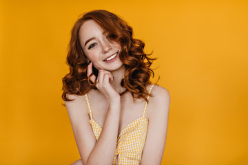 Indoor portrait of lovely red-haired woman enjoying photoshoot on yellow background. Studio shot of cheerful european girl with curly ginger hair.