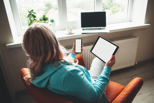 Senior woman sitting in the armchair with a tablet and phone while looking at the laptop