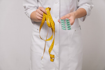 Women's hands hold a centimeter ribbon and pills for weight loss. The concept of a dietitian