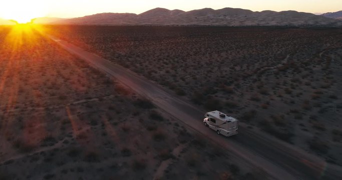 AERIAL - A camper drives towards a sunset in the middle of the Mojave desert on a sand road on a summer day