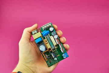 Power supply Board on pink background, top view. A person holds a printed circuit Board (PCB) with capacitors and diodes.