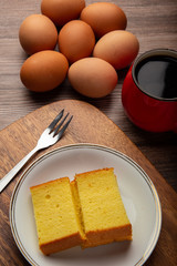 Plate with delicious sliced butter cake with cup of coffee and fresh egg on wooden background.