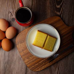 Plate with delicious sliced butter cake with cup of coffee and fresh egg on wooden background.