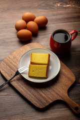 Plate with delicious sliced butter cake with cup of coffee and fresh egg on wooden background.