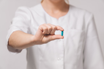 A girl doctor in a white robe holds a capsule with closeup medicine