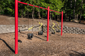 Closed playground swing set on a sunny day, closed and taped off due to Covid 19
