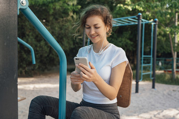 Girl brunette with blue eyes in a white top looks into the mobile phone and listens to music middle plan