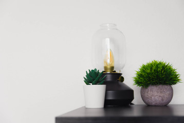 Black desk with an Edison lamp and succulents in the corner, against a white wall. Room for Text. Scandinavian style.