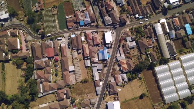 Aerial top down view of a small town in the countryside with Y intersection road. Rooftop of town houses, curve road with few vehicles and field farms. Rural tropical countryside.