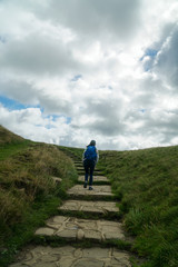 A female hiker walking up the hill with a blue backpack in Peak District National Park in the UK