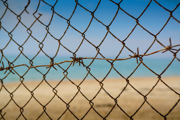 Steel mesh and barbed wire on a background of blurry sea and beach