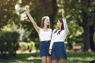 Beautiful girls in a jeans skirts. Women in a summer park. Friends with ice cream