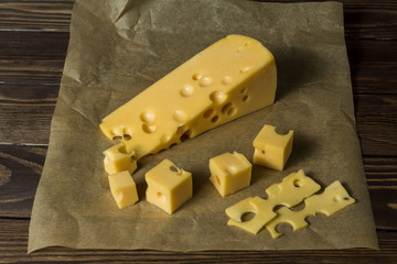 Maasdamer cheese. diced cheese in wrapping paper on an old black wooden table.