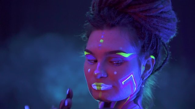 Portrait of a Girl with Dreadlocks in Neon UF Light. Model Girl with Fluorescent Creative Psychedelic MakeUp, Art Design of Female Disco Dancer Model in UV, Colorful Abstract Make-Up. Dancing Lady
