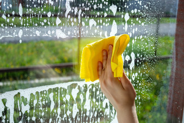 The girl washes the window with cleaning products and a rag. House cleaning