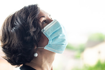 Girl in a medical mask against a white sky look up