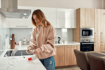 Change the way you feel. Young woman getting cannabis buds out of a plastic bag for grinding it up using red marijuana grinder. Glass water pipe or bong on the table. Cannabis legalization concept