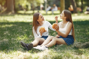 Beautiful girls in a jeans skirts. Women in a summer park. Friends with a burgers