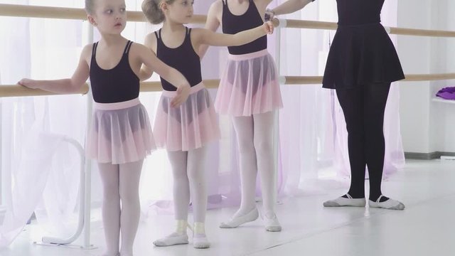 Little girls are having classical ballet lesson learning leg movements with teacher in art studio.