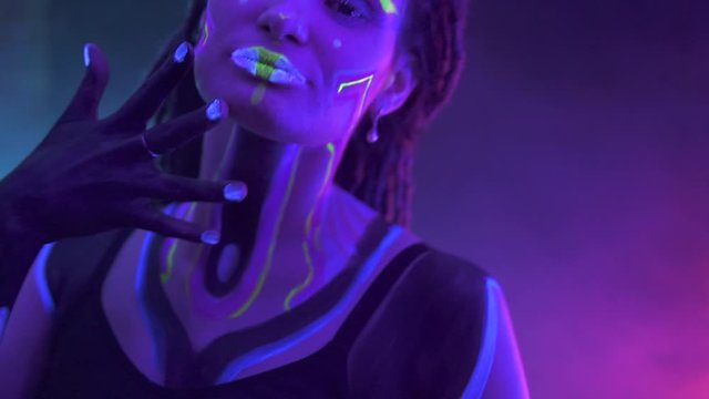 Portrait of a Girl with Dreadlocks in Neon UF Light. Model Girl with Fluorescent Creative Psychedelic MakeUp, Art Design of Female Disco Dancer Model in UV, Colorful Abstract Make-Up. Dancing Lady