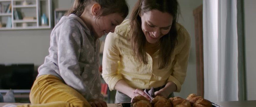 Mother and daughter cooking together at home, taking out bakery from the oven in the kitchen
