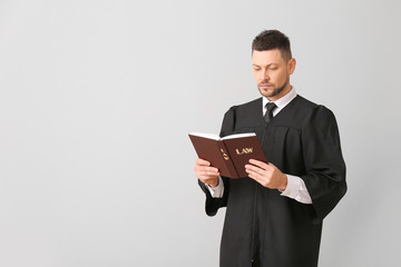 Male judge with book on light background
