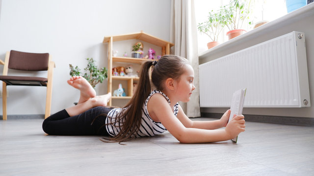 Distance learning. Little girl lying on a wooden floor with a book