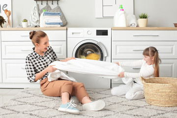Woman and her cute little daughter having fun while doing laundry at home