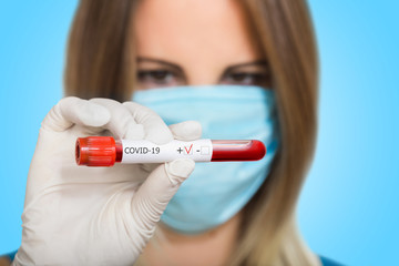Nurse doctor in medical mask holding test tube with positive coronavirus test blood sample