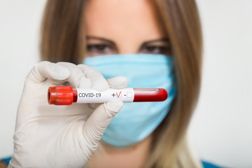Nurse doctor in medical mask holding test tube with positive coronavirus test blood sample