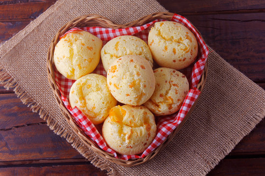 homemade cheese bread, traditional Brazilian snack, in a heart-shaped basket on a rustic kitchen table