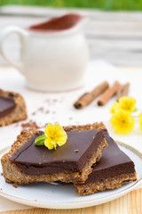Сhocolate tart made from oatmeal, coconut milk and butter, dates and almonds on a white saucer.Cinnamon sticks and yellow flowers in the white background.Сoncept of healthy food and healthy dessert