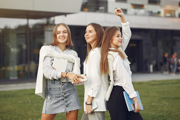 Students in a park. Girls on a campus. Friends with a phone. - obrazy, fototapety, plakaty