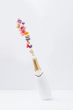 Creative concept with white champagne bottle and colorful natural spring flowers. Minimal celebration or party background.