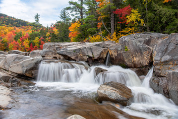 Beautiful waterfall along a mountain river on a cloudy autumn day. Stunning autumn colours in...