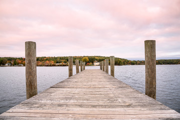 Deserted wooden pier on a lake with forested shores at dusk. Beautiful fall foliage. Lake Winnipesaukee, NH, USA.