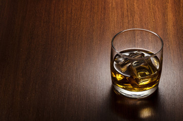 Glass of whiskey on the rocks, positioned on the ridht side of the composition, isolated on wooden background