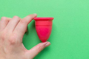 Close up of woman hand holding menstrual cup over green background. Women health concept, zero...