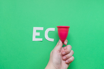 Close up of woman hand holding menstrual cup over green background. Women health concept, zero...
