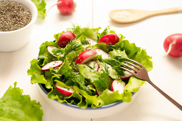 A plate with vegetarian salad stands on a wooden table. Salad of radish, lettuce, herbs and chia and sesame seeds seasoned with vegetable oil.