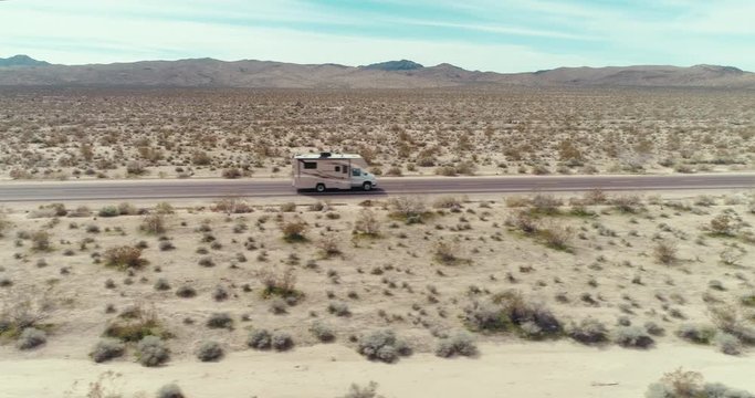 AERIAL - A drone slowly follows an RV that drives through the image from left through right in the Mojave Desert on a sunny day