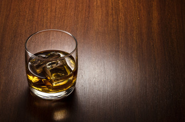 Glass of whiskey on the rocks, positioned on the left side of the composition, isolated on wooden background