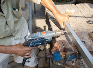 The handyman using drill to creation of metal parts on wood table for his work.
