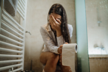 Sad woman on the toilet with toilet paper,suffering from abdominal pain.Female health problem with...