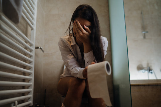 Disappointed woman on the toilet with toilet paper,suffering from abdominal pain.Female health problem with digestion and reproductive system.Constipation /menstrual cramps.Bowel movement issues.