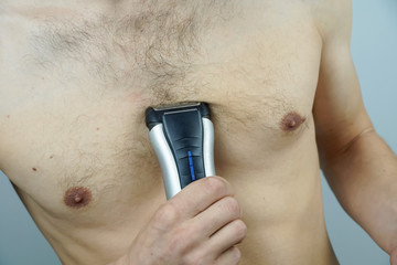 Close-up of a naked man using an electric razor to remove hair from his chest