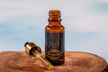 A bottle of propolis on piece of wood Propolis Drop Oil drop falling - obrazy, fototapety, plakaty